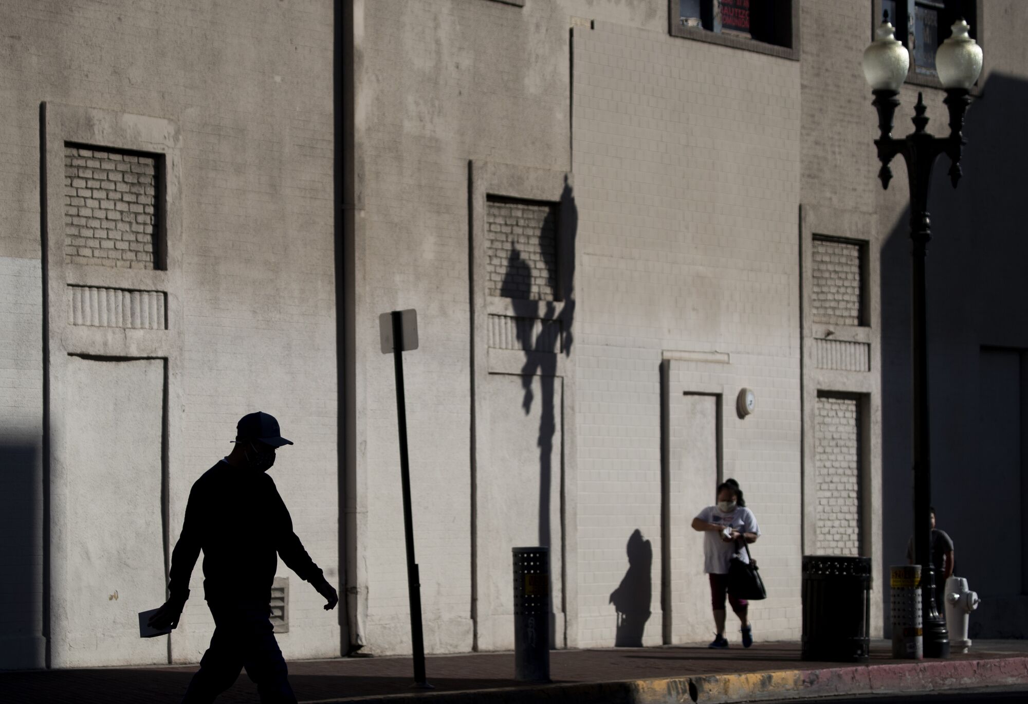 Shadows cast against a gray wall by pedestrians and street signs