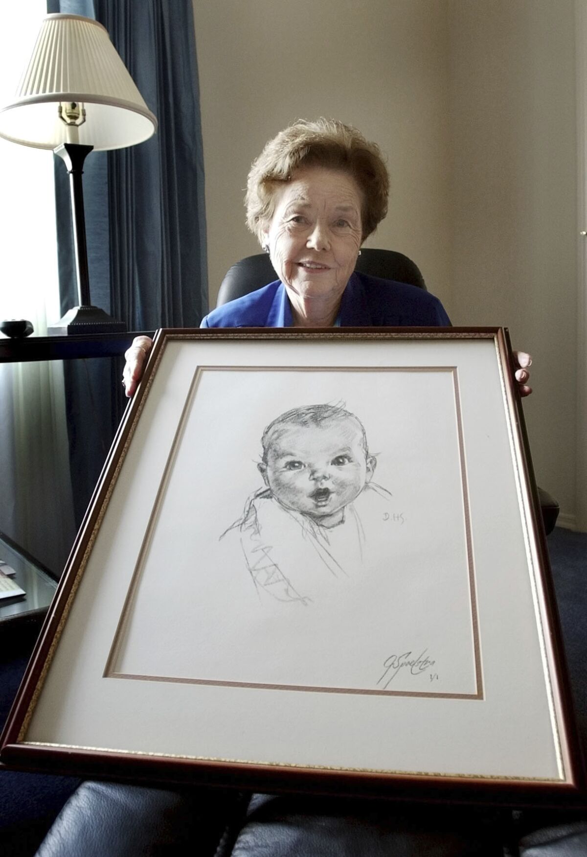FILE - Ann Taylor Cook, poses at her Tampa, Fla., home Wednesday afternoon Feb. 4, 2004, with a copy of her photo that is used on all Gerber baby food products. Ann Turner Cook, whose cherubic baby face was known the world over as the original Gerber baby, has died. She was 95. Gerber announced Cook's passing in an Instagram post on Friday, June 3, 2022. (AP Photo/Chris O'Meara, File)