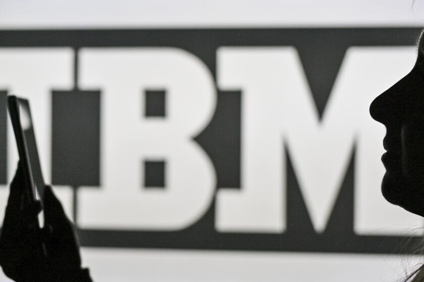 An image of a woman holding a cell phone in front of the IBM logo displayed on a computer screen. On Tuesday, January 12, 2021, in Edmonton, Alberta, Canada. (Photo by Artur Widak/NurPhoto via AP)