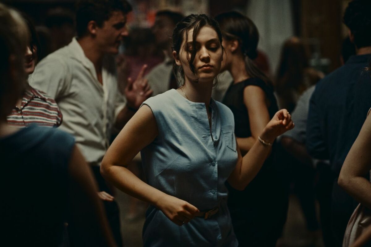A woman in a blue linen dress moves through a crowd, looking like she's dancing  