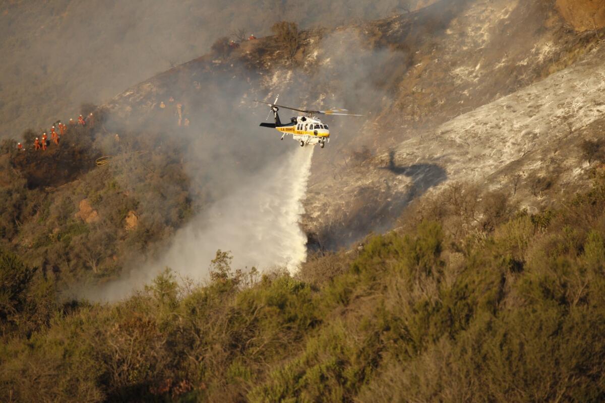 A firefighting helicopter makes a water drop on a brush fire in Malibu, where a fire crew inmate battling the blaze suffered fatal injuries Thursday.