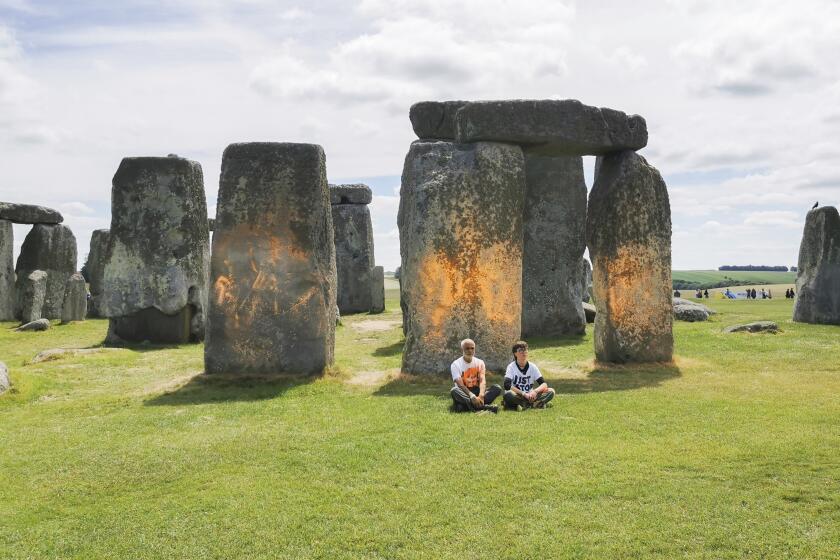 In this handout photo, Just Stop Oil protesters sit after spraying an orange substance on Stonehenge, in Salisbury, England, Wednesday June 19, 2024. (Just Stop Oil via AP)