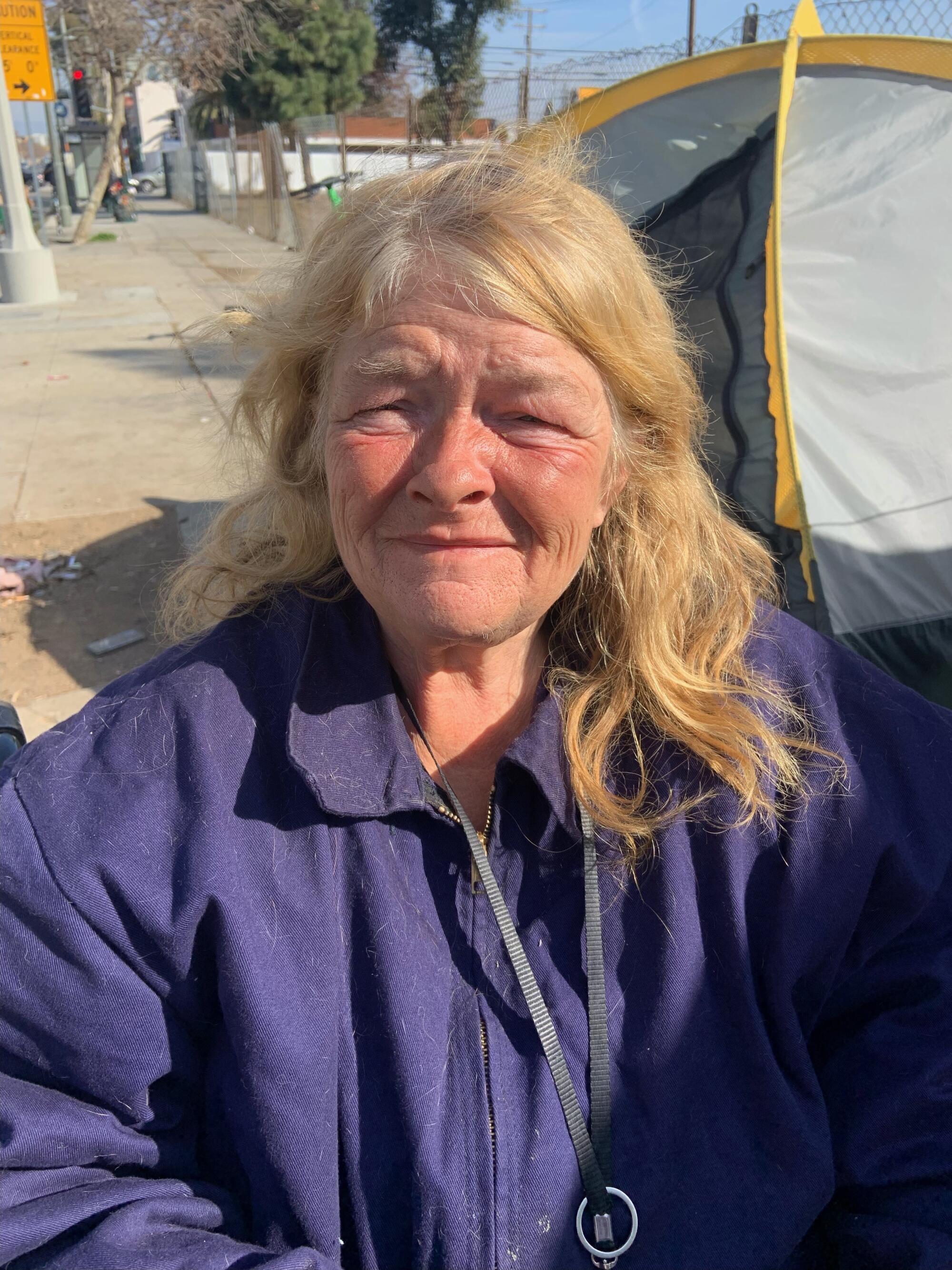 A woman in a purple jacket and a tent in the background.