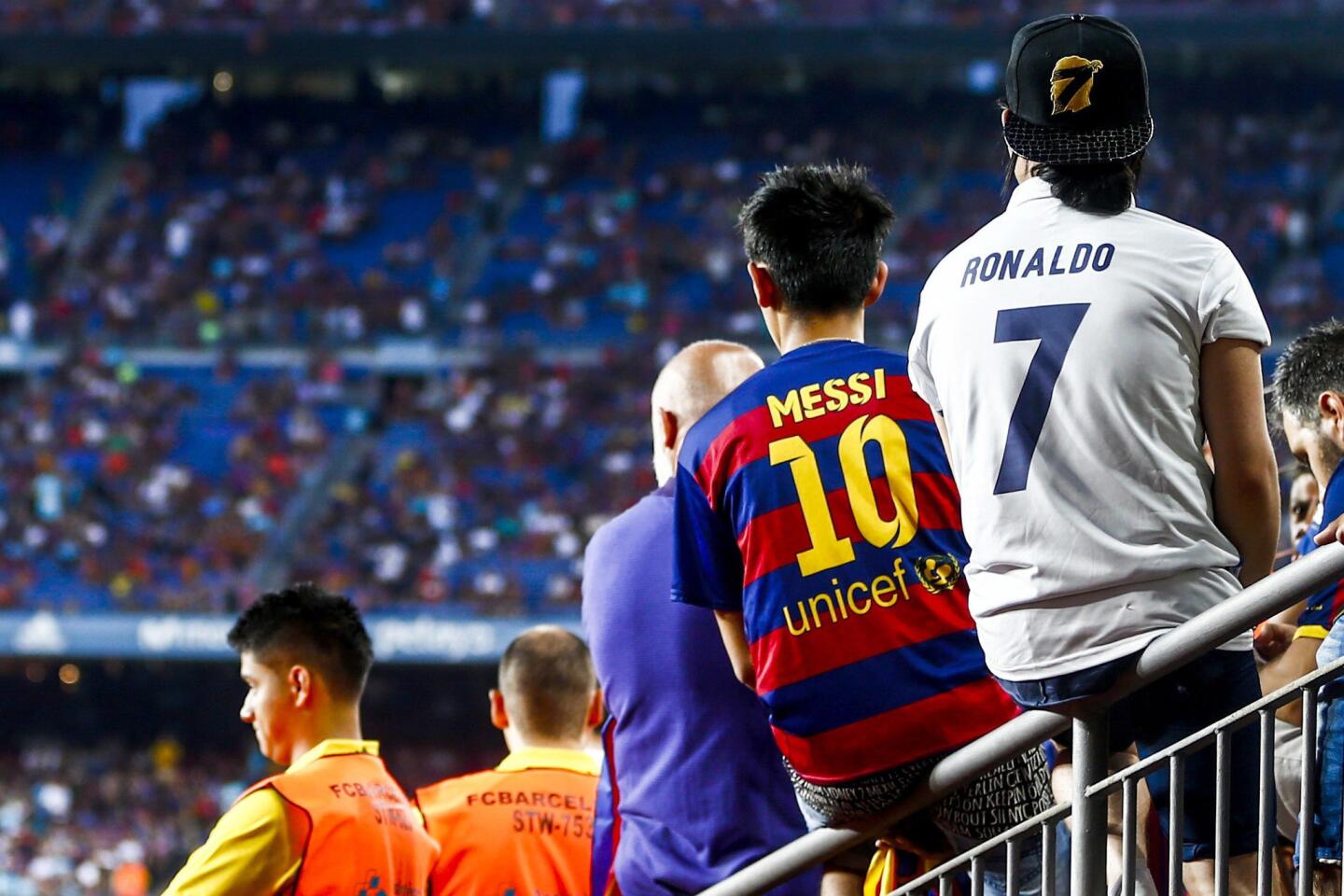 Unos aficionados con camisetas de Messi y Ronaldo esperan a que comience el partido de ida de la Supercopa de España en el Camp Nou. EFE