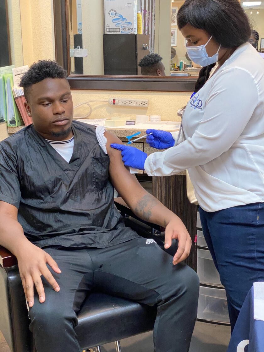 An unmasked man gets a vaccine injection at a barber shop