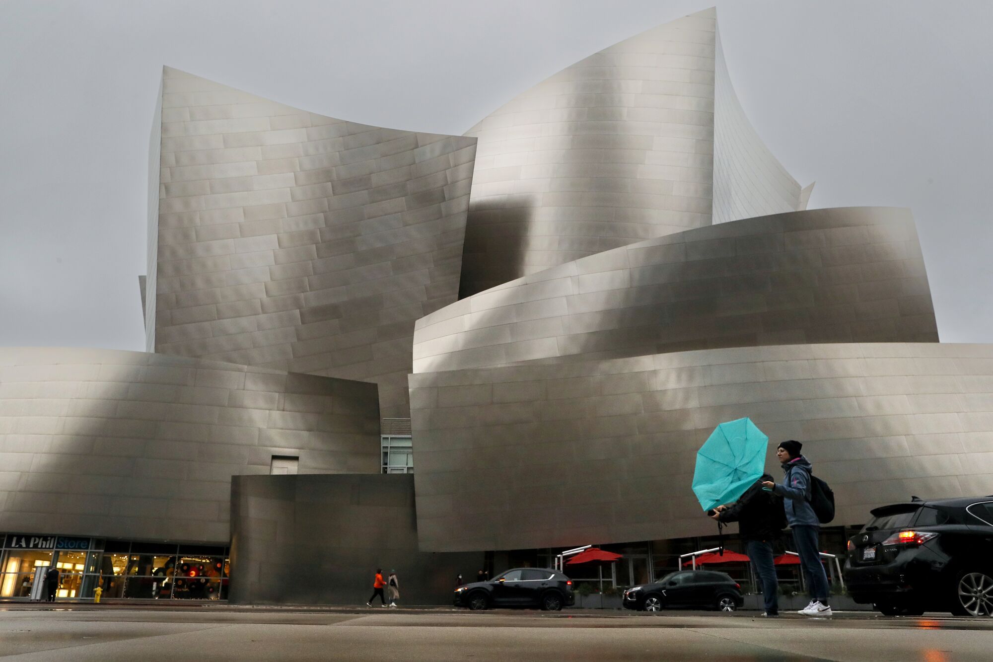 Two people stand with a bent umbrella outside Walt Disney Concert Hall