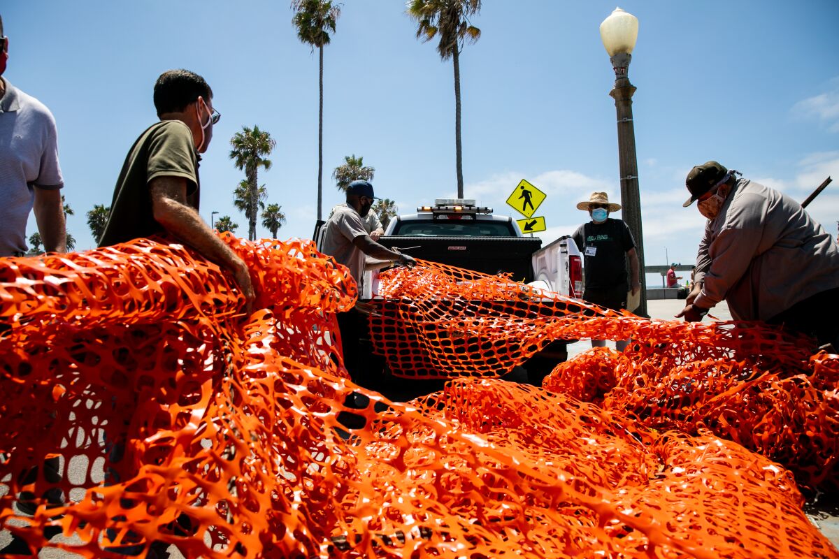 City crews haul away a fence that had been put up to prevent gathering at Ocean Beach Veterans Plaza