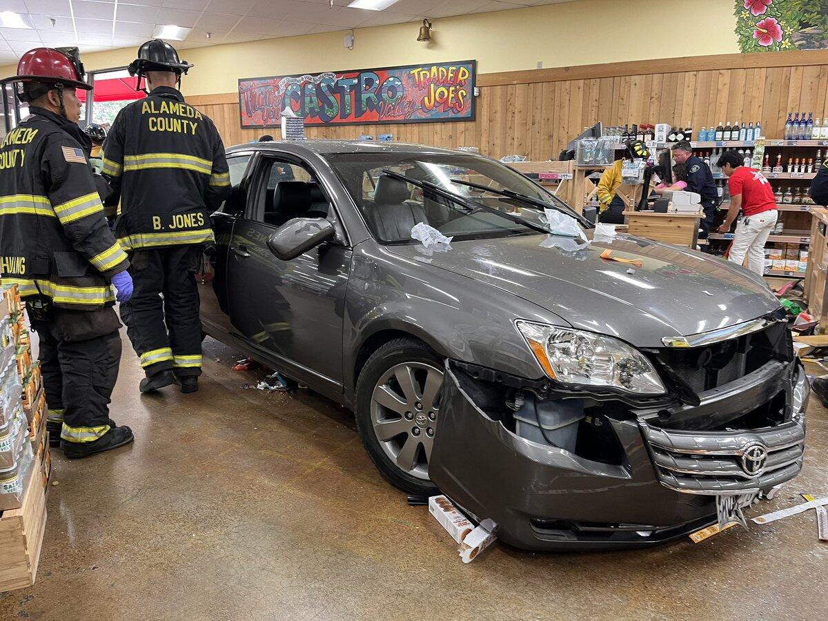 A silver Toyota sedan crashed inside a grocery store, with firefighters standing next to it