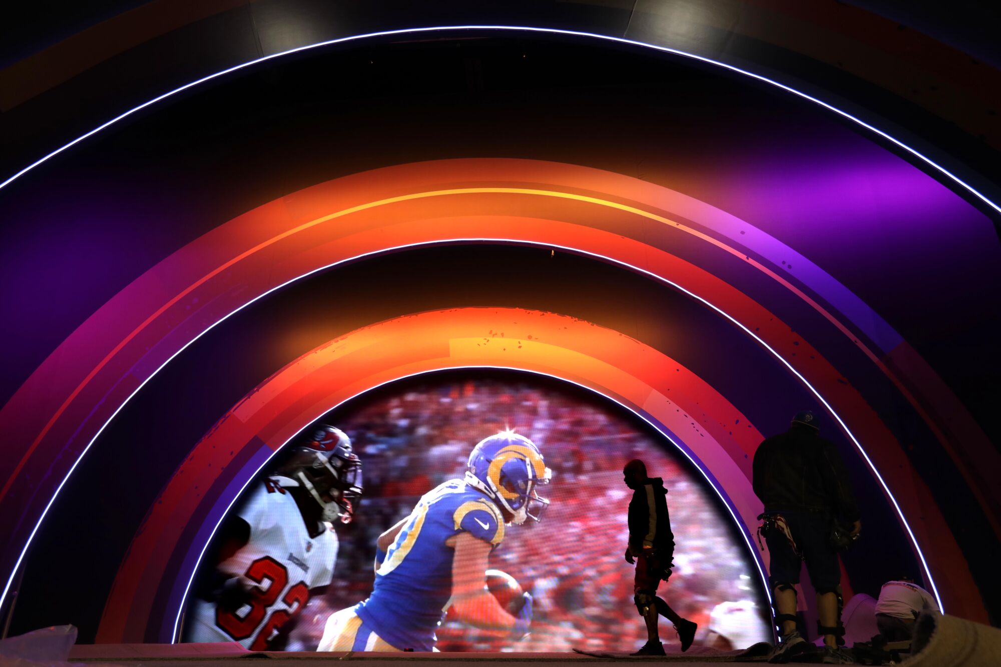 A worker preps the main stage while a video of a Rams game is screened 