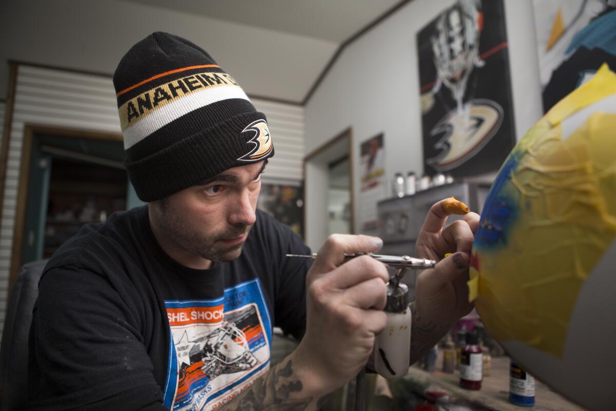 Noah Ennis, a helmet and hockey mask painter, works on a design in his shop, Shell Shock Custom Paint, in Fairbury, Neb.