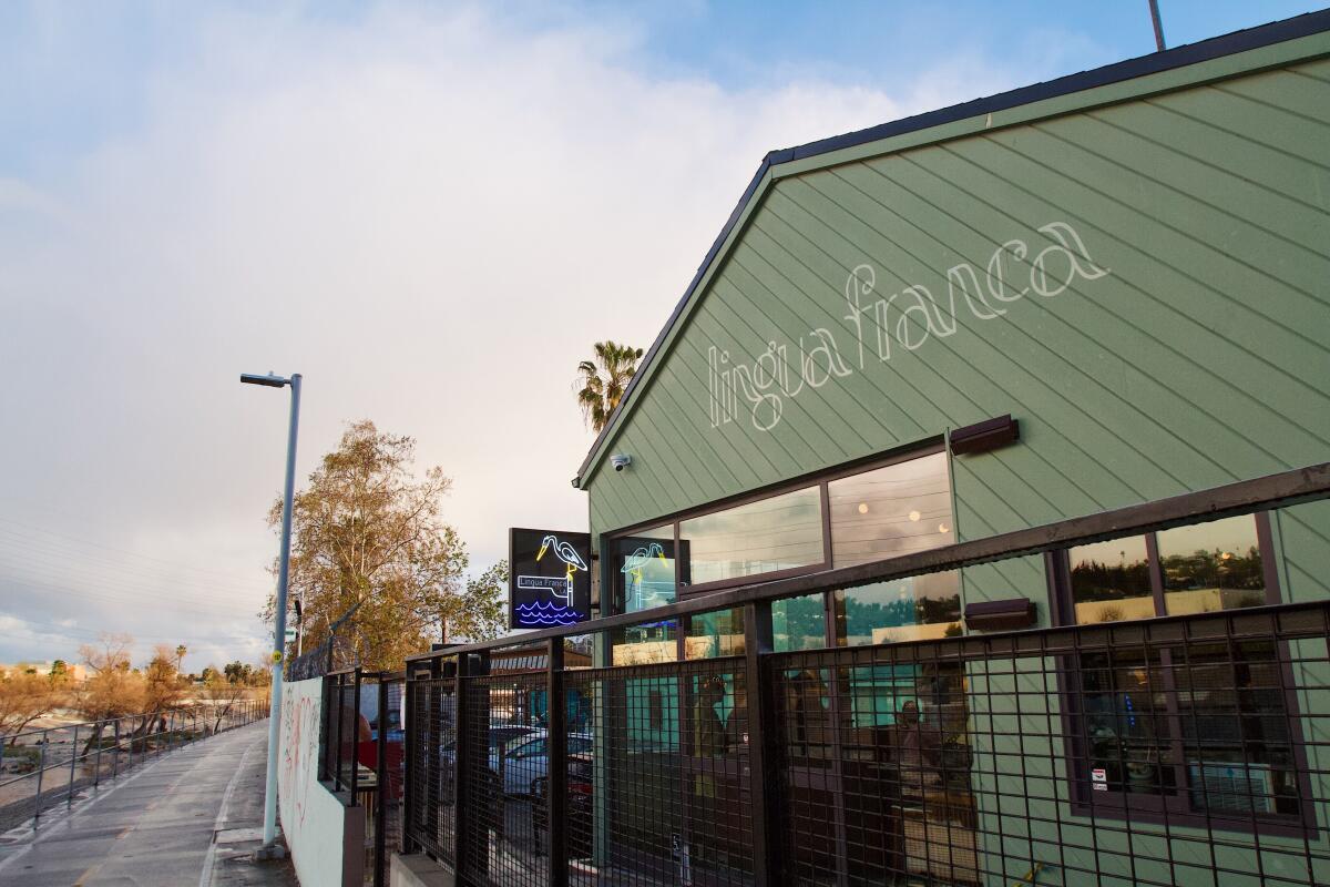 A restaurant exterior with diagonal green wooden planks and the words Linga Franca. It's by a bike path and the L.A. River.