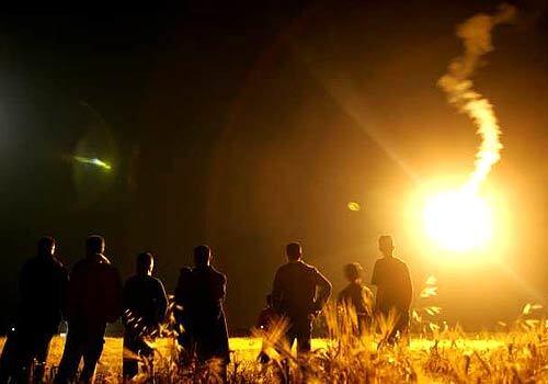 The sky is lit by an Israeli flare as Palestinians wait for the bodies of militants from Al Aqsa Martyrs' Brigades killed near the Gaza-Israel border.