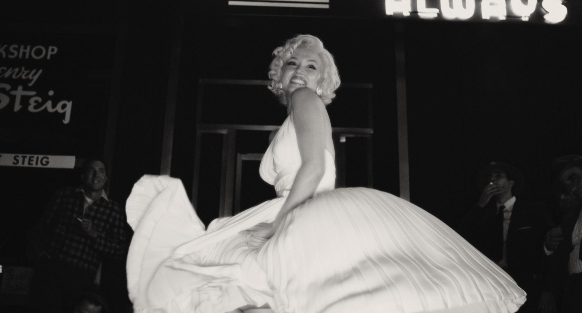 A black-and-white image of a blond woman posing in a billowing, white dress