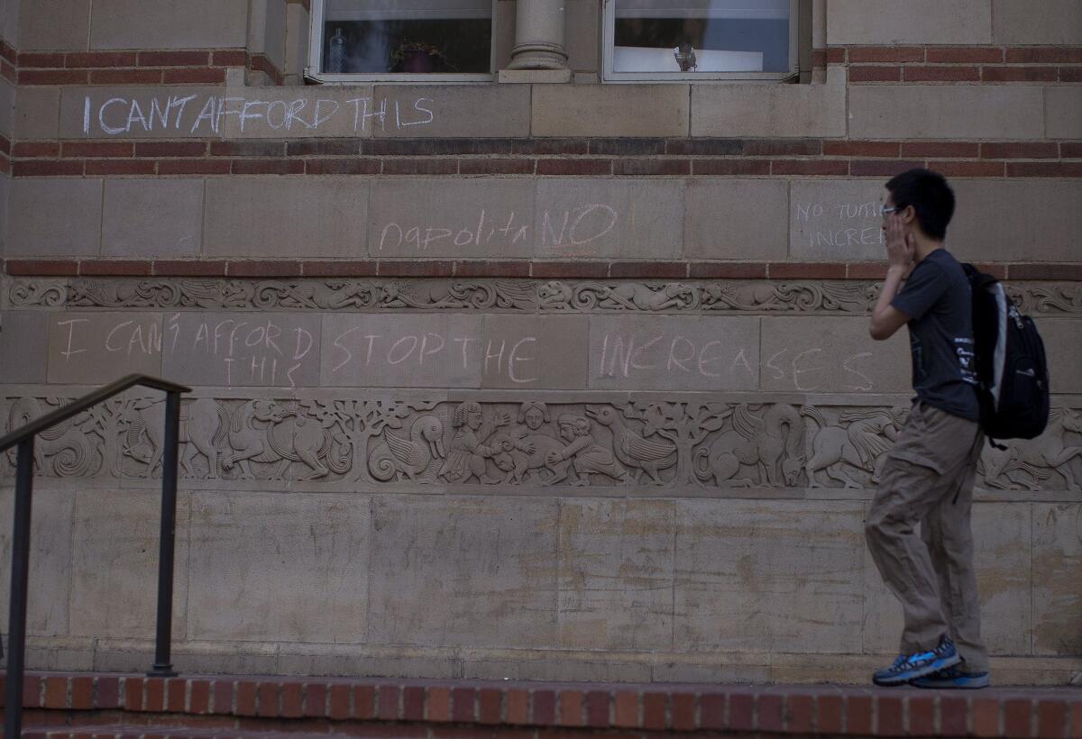 A student walks past a chalk-written protest against tuition hikes on the wall outside Powell Library at UCLA on Tuesday.