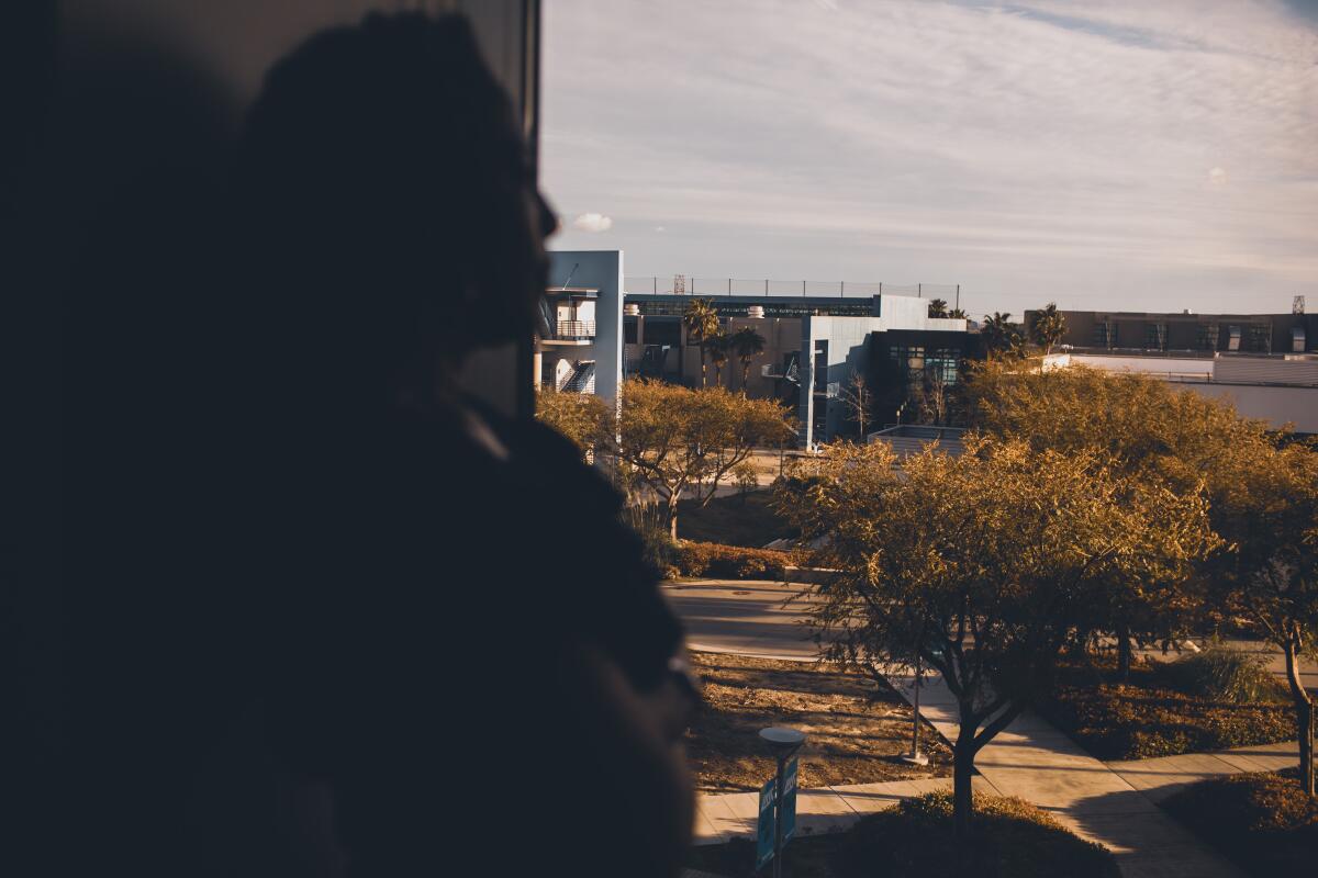 A woman seen in silhouette looking out a window at trees and buildings on a campus