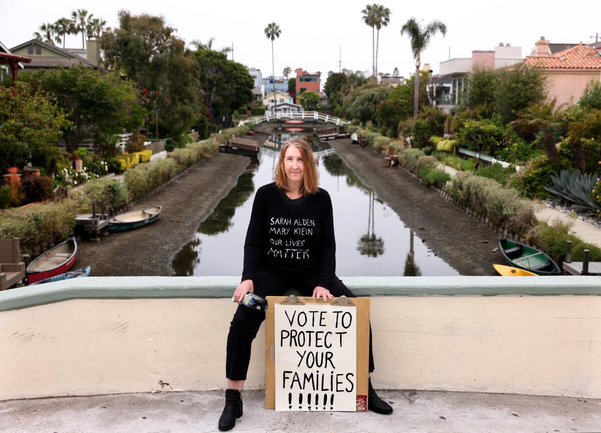 Mary Klein poses with a political poster sitting on a bridge at the Venice Canals