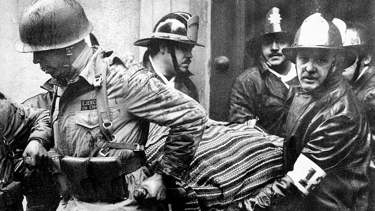 The body of President Salvador Allende, wrapped in a Bolivian poncho, is carried by soldiers and firefighters from the destroyed presidential palace after the Sept. 11, 1973, coup that ended Allende's three-year government.