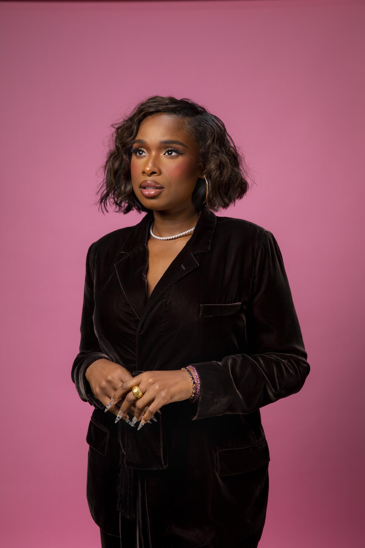 A woman wearing black and pictured against a pink backdrop.