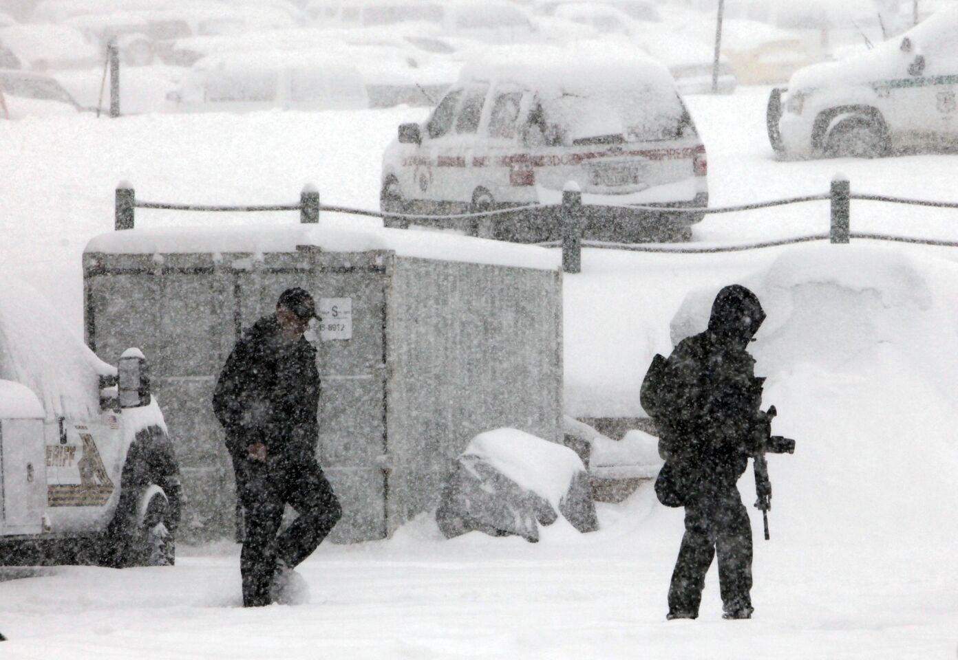 Police teams armed with assault rifles walk through falling snow at the San Bernadino County sheriff's command post at the base of Bear Mountain.