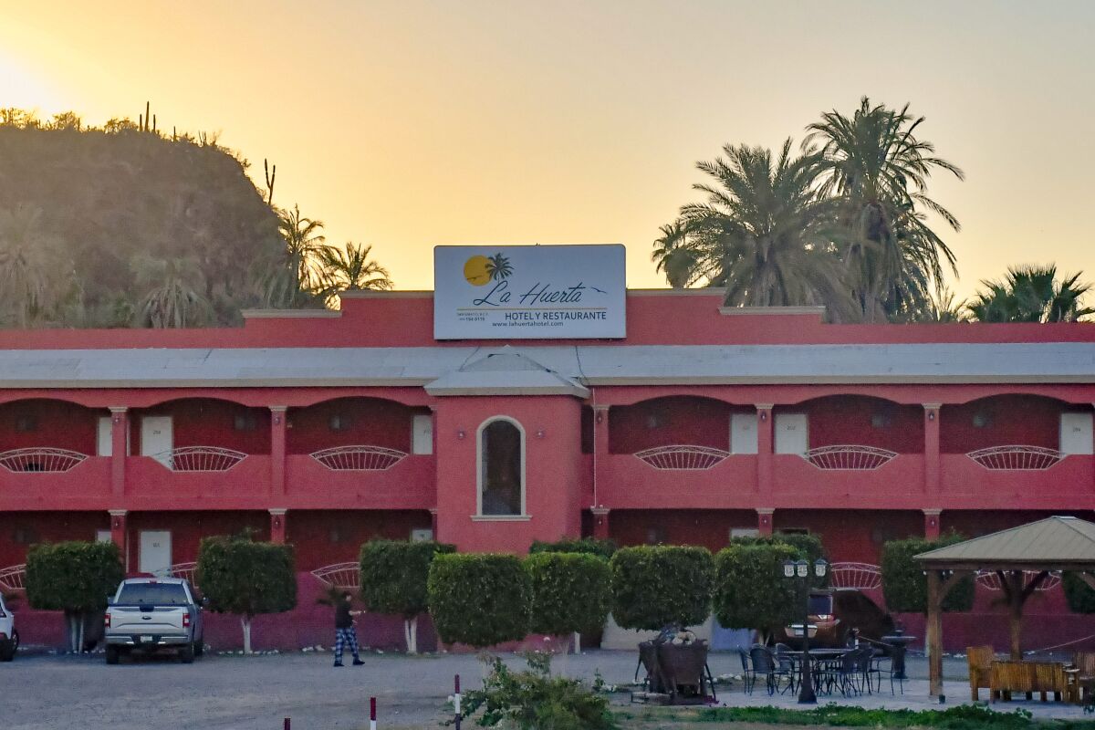 A pink hotel with palm trees and the setting sun behind it