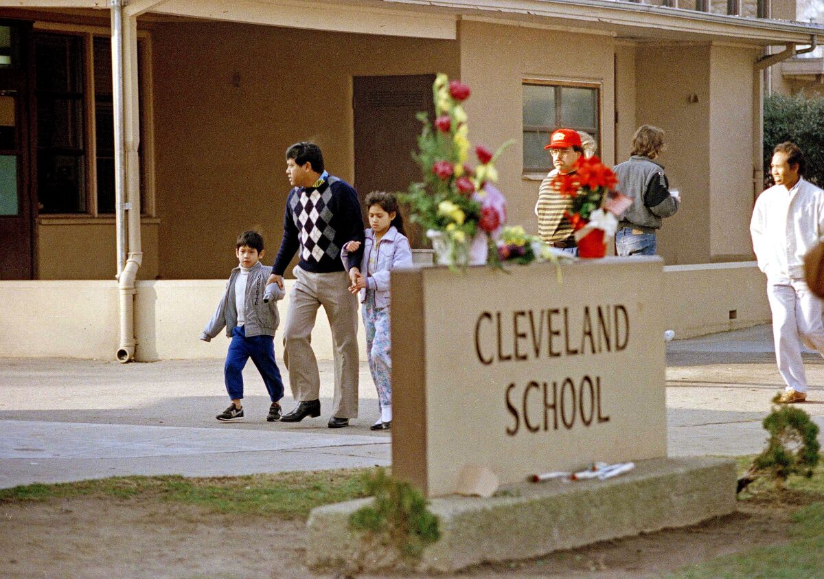 A man and two children walk behind a sign that says Cleveland School with flowers on top of it