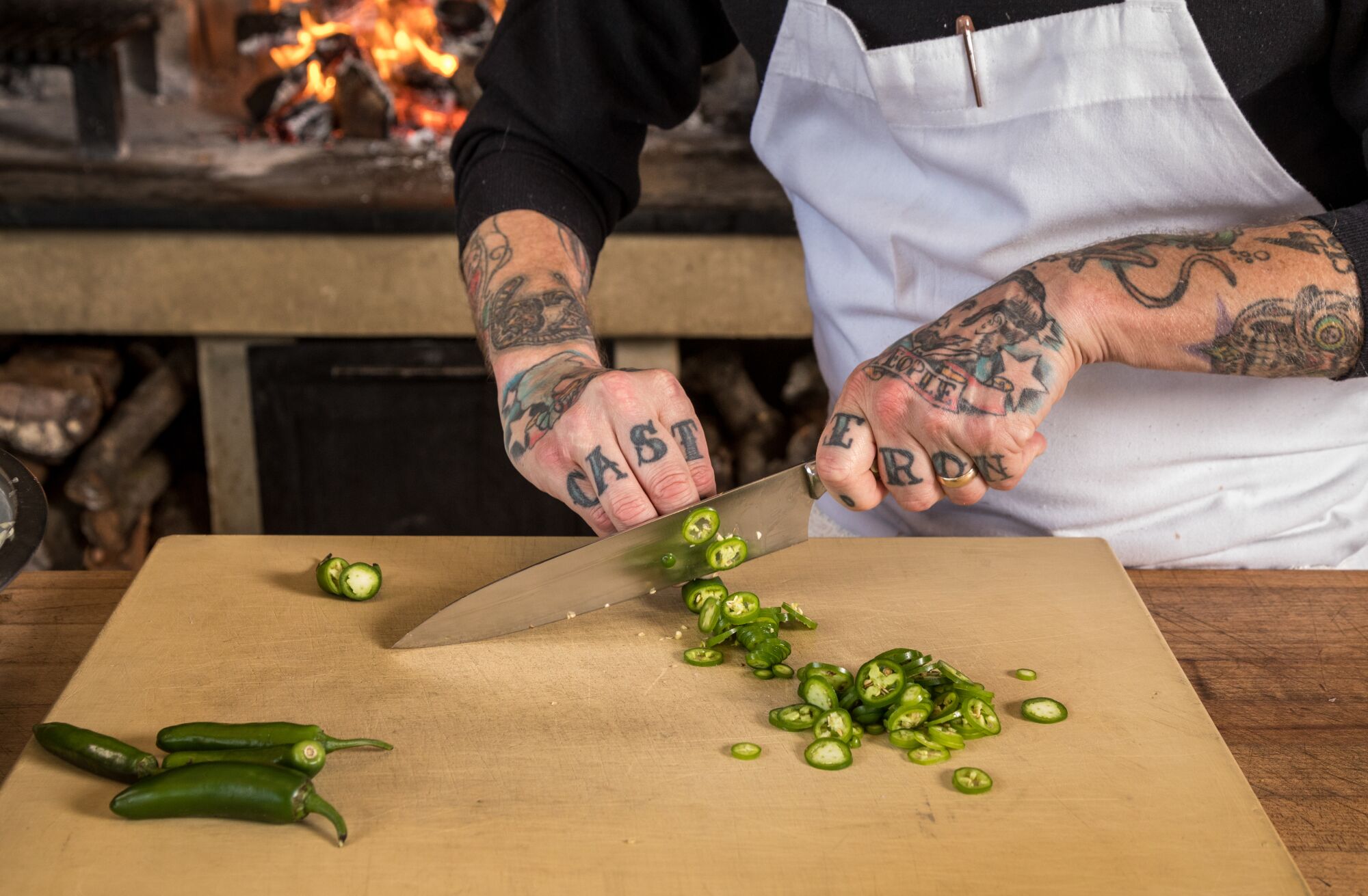 A pair of tattooed hands chops green chilis.