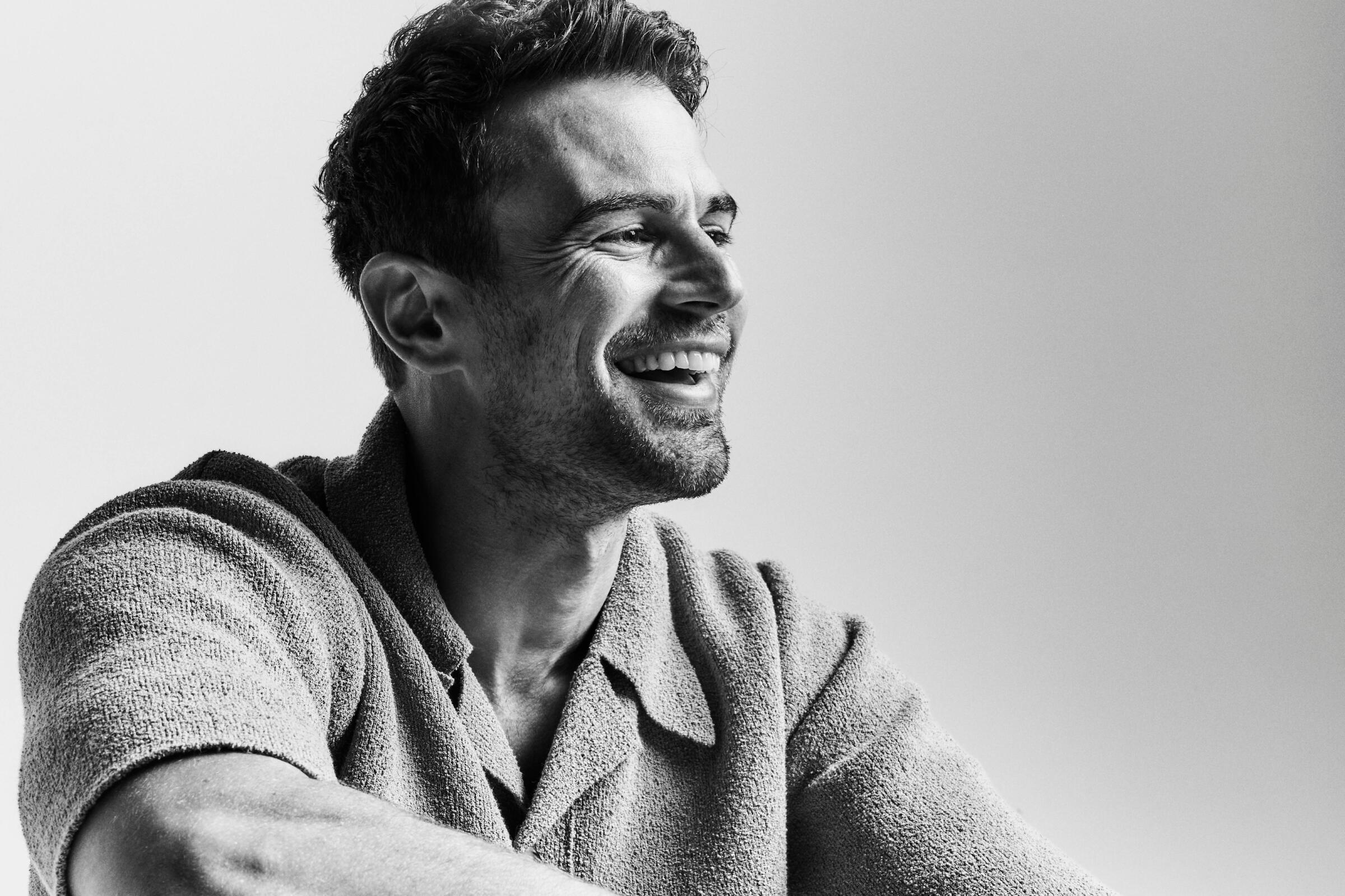 Theo James smiles in a black-and-white profile portrait.
