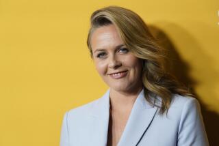 Alicia Silverstone smiles in a light blazer against a bright yellow background