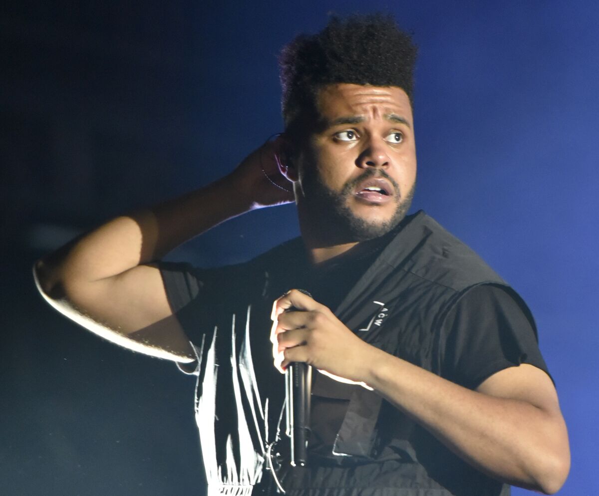 The Weeknd holds a microphone on stage.