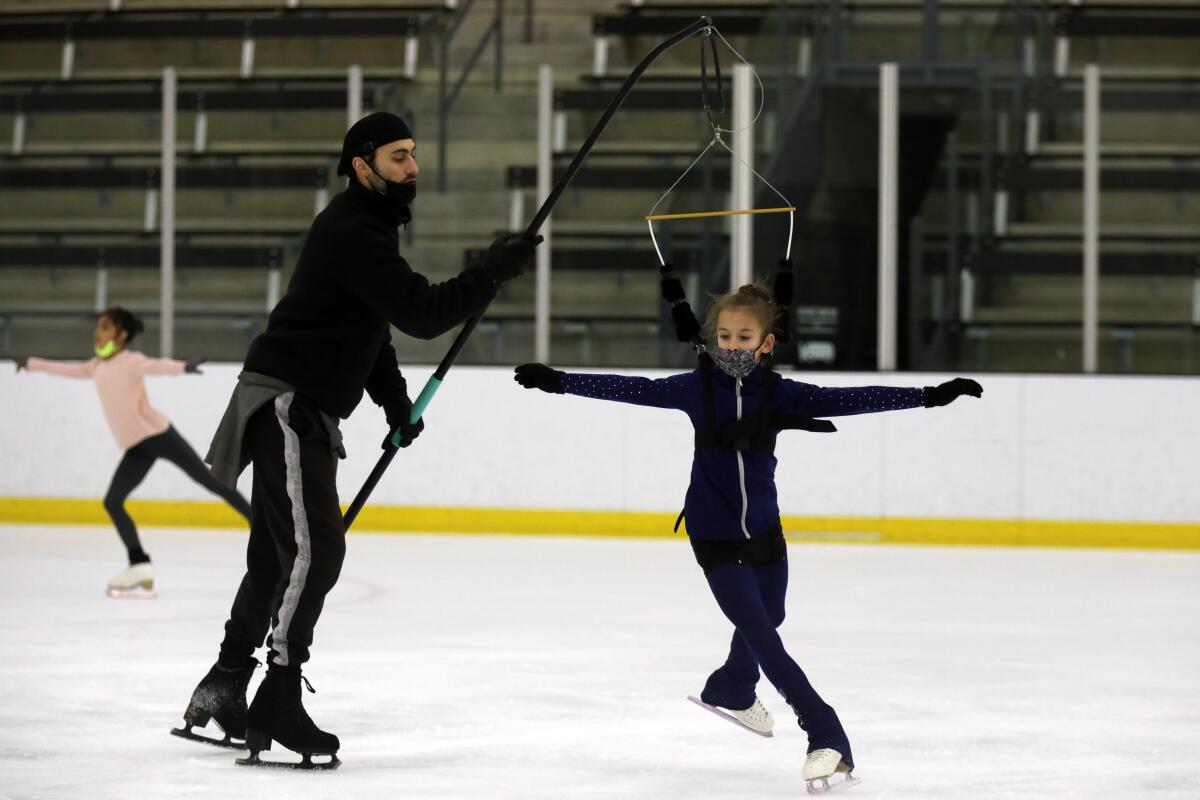 A figure skating coach holds a pole attached to a harness where a figure skater practices jumping.