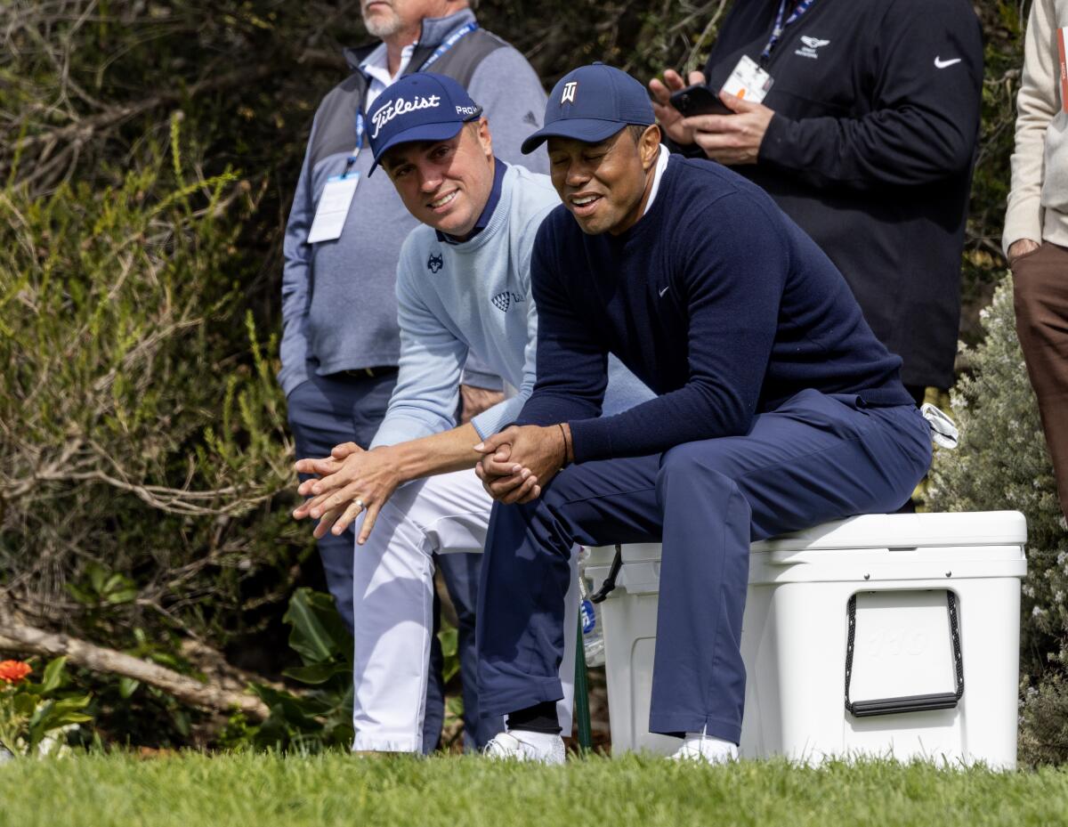 Justin Thomas, left, and Tiger Woods take a break on an ice chest at the 4th tee box