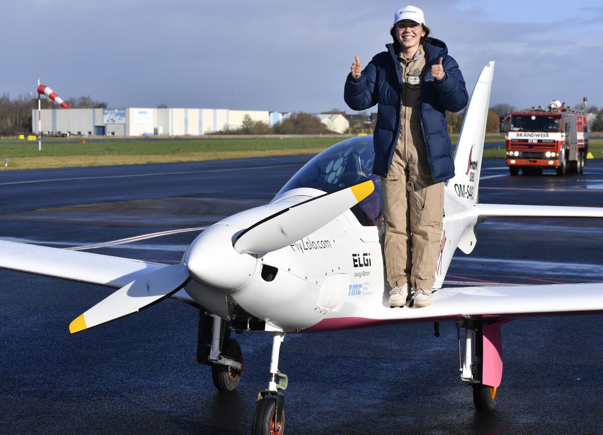 Pilot Zara Rutherford stands on a wing of her parked plane and gives thumbs up.