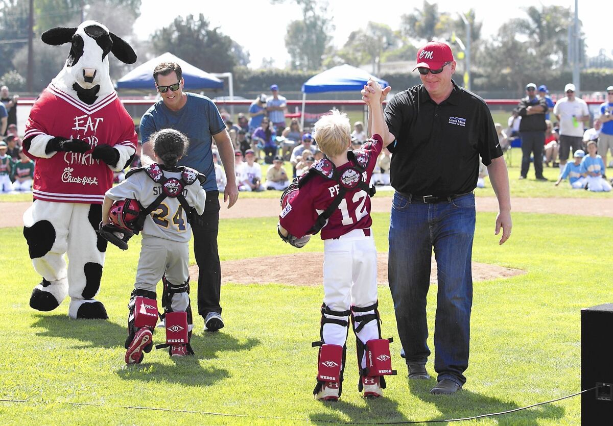 Costa Mesa mayor Steve Mensinger, right, and former major league player Chad Kreuter, left, high-five two players after they threw in the first pitches during the Costa Mesa National Little League opening day ceremonies at Tewinkle School on Saturday.