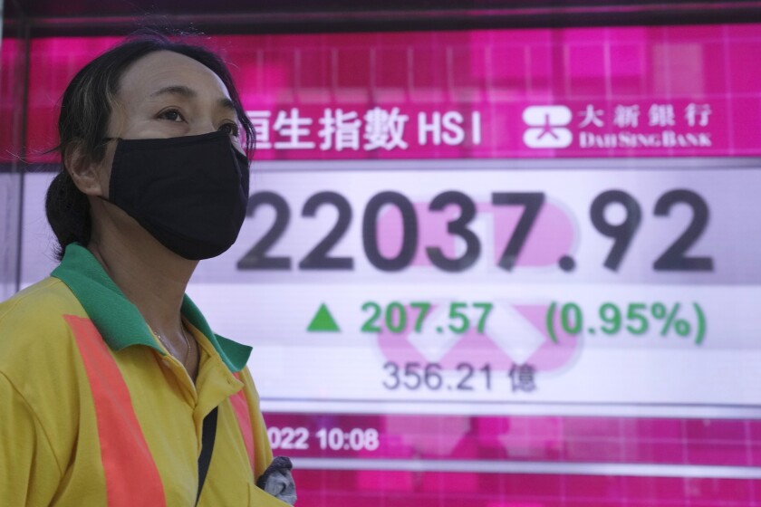 A woman wearing a face mask walks past a bank's electronic board showing the Hong Kong share index in Hong Kong, Tuesday, July 5, 2022. (AP Photo/Kin Cheung)