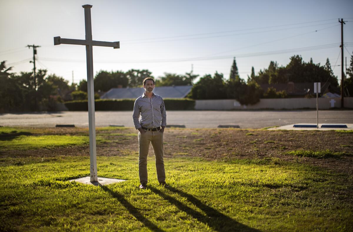 Housing developer Kyle Paine stands on a grassy area next to a white cross.