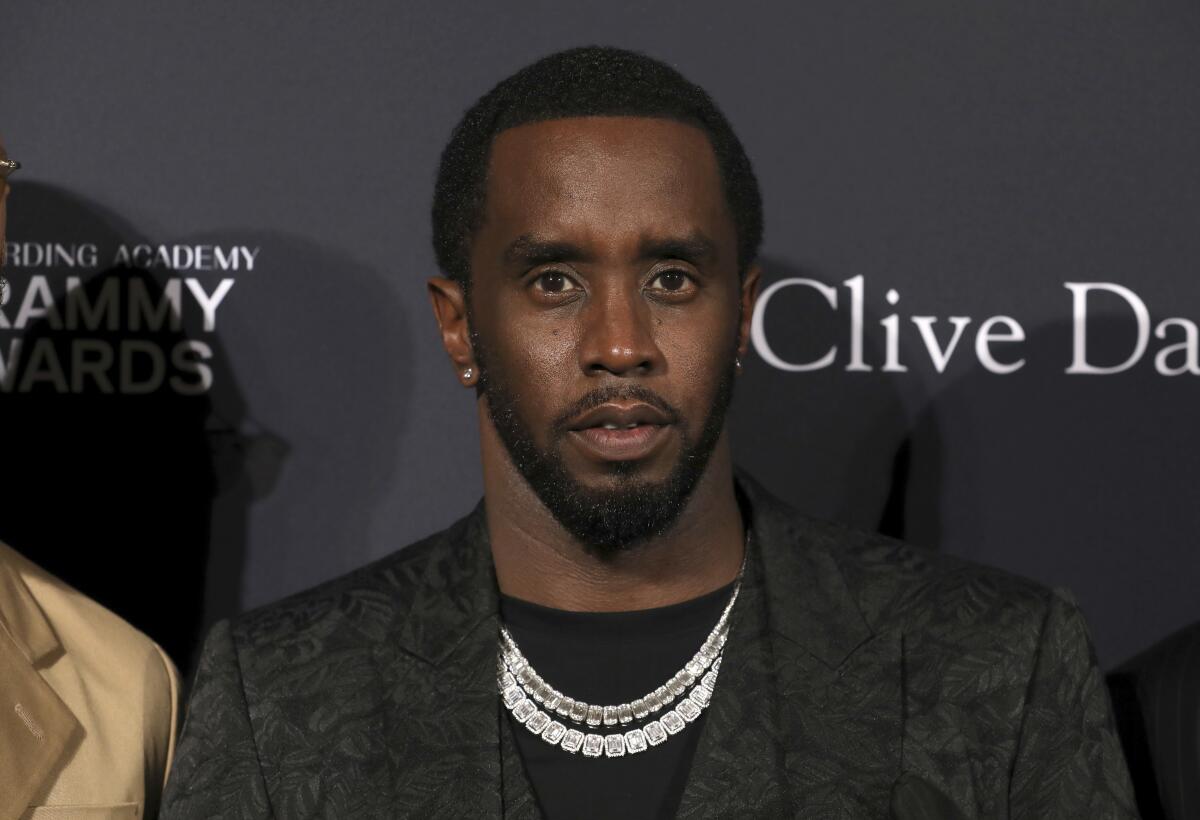 Sean "Diddy" Combs in a black blazer, black shirt and chains looking ahead as he poses at a red carpet