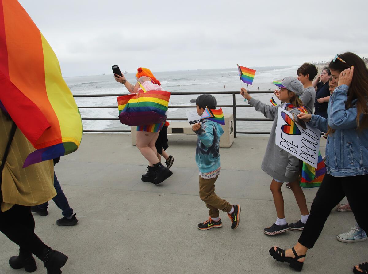 Local activists of all ages and LGBTQ+ supporters walk to the end of Huntington Beach pier to hang a giant Pride flag Sunday.