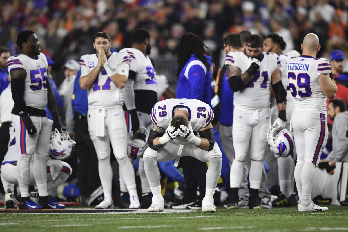 Football players stand on the field looking stunned.