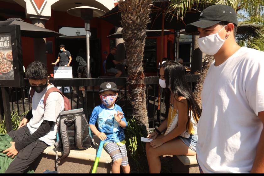 HUNTINGTON BEACH, CA - AUGUST 12, 2020 - -Richard Hernandes, from right to left, his girlfriend Jazmin Domingo, his brothers Seth Patlan, 5, and Joseph Hamassian, all wearing masks, wait for a table at a restaurant along Main Street during a "Masks Up, Surf City," banner campaign to prevent coronavirus in the city of Huntington Beach on August 12, 2020. The campaign, a play on the phrase "Surf's Up," includes 100 pennants, a banner at the pier and digital displays citywide, Huntington Beach spokeswoman Catherine Jun said. Fifty pennants were installed downtown on Aug. 6. The remaining signs are in production this week, and 13 pennants and a banner are expected to be installed on the Huntington Beach Pier. Huntington Beach. (Genaro Molina / Los Angeles Times)