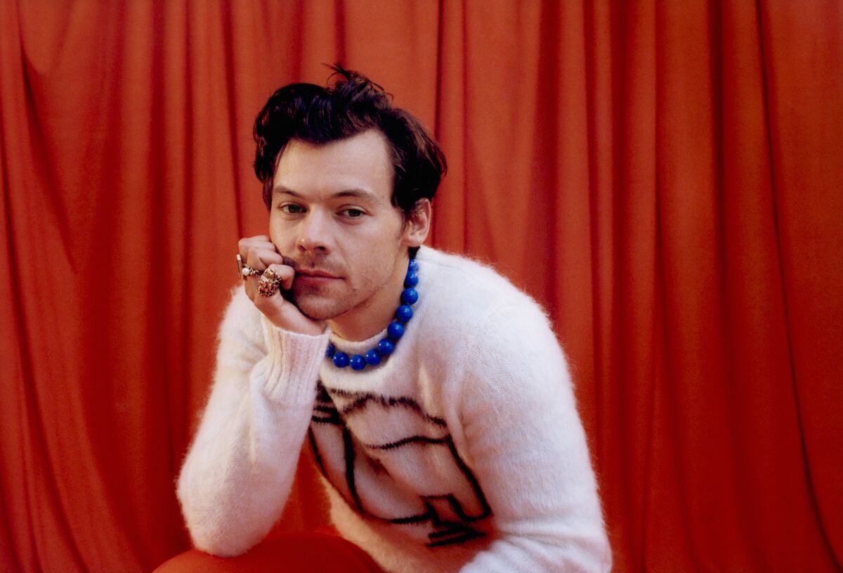 A man wearing a sweater and resting his chin on his palm in front of a red background