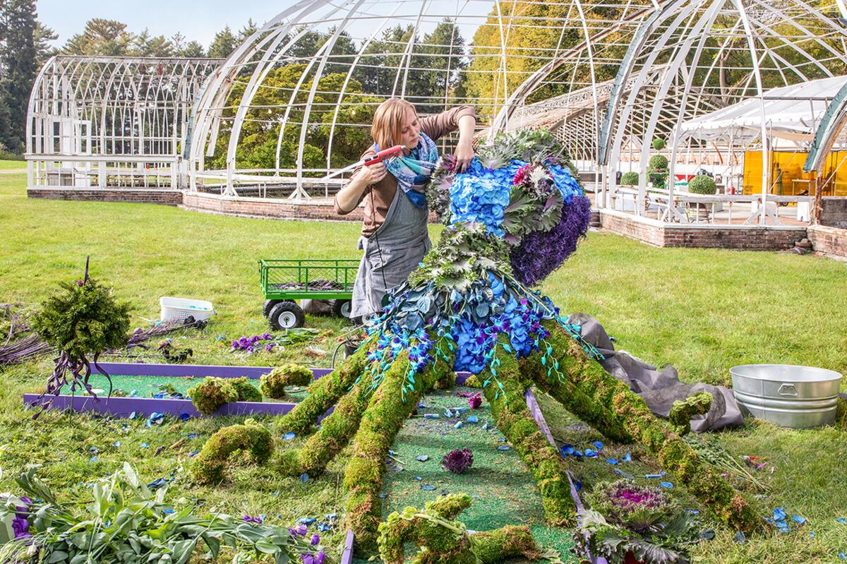 A woman works on an ornate, flowered topiary in the shape of an octopus, to accompany a mini golf hole