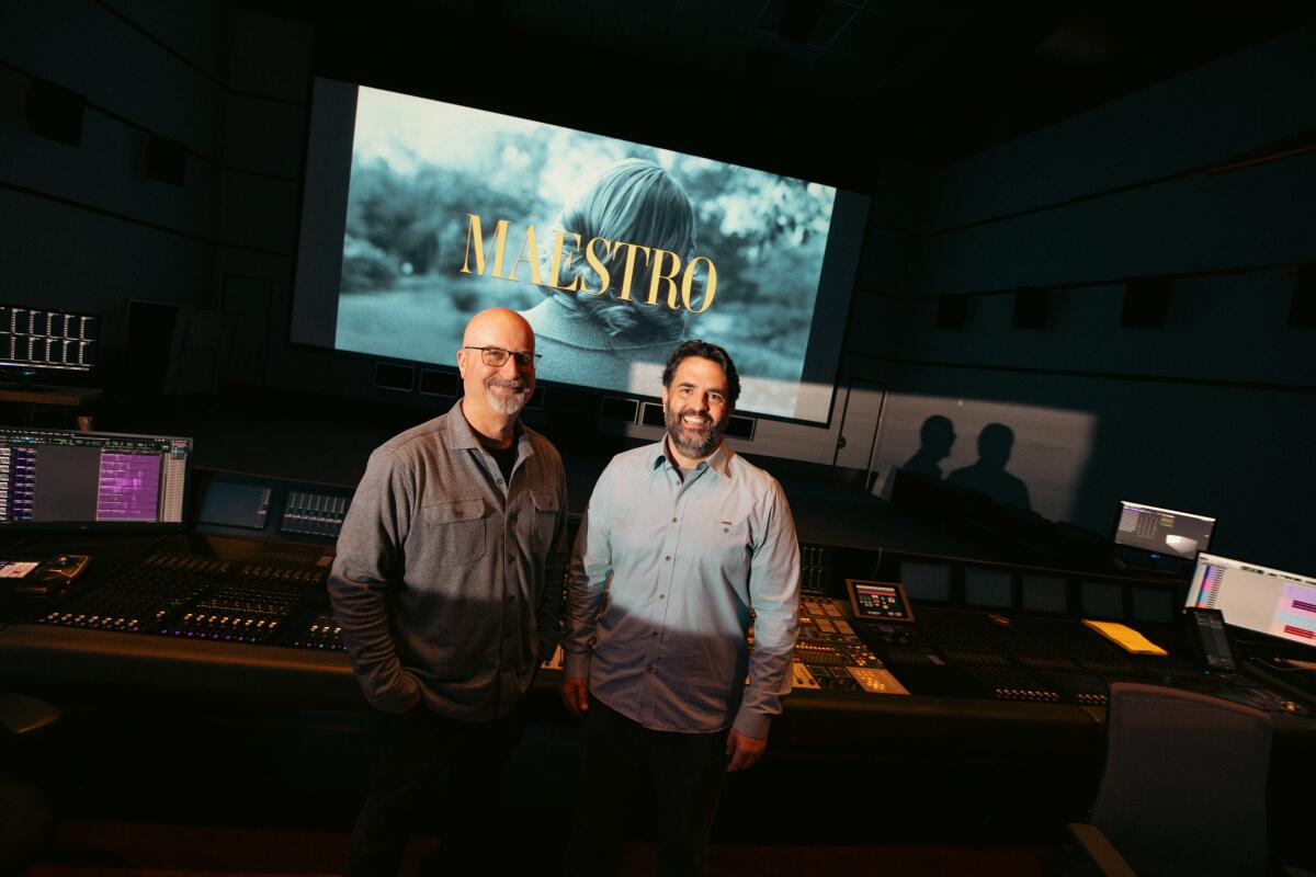 Two men stand in a work space with "Maestro" on a screen behind them.