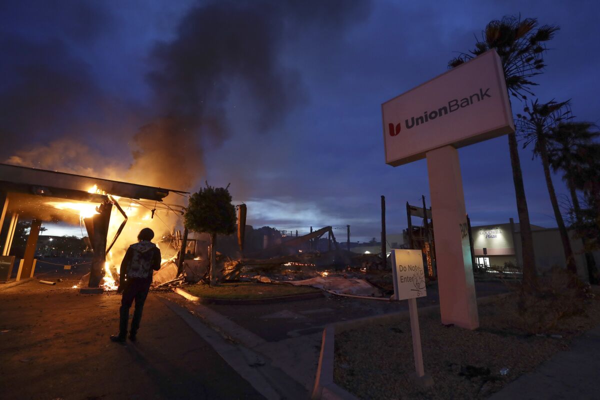 FILE - A man looks on as a bank burns after a protest over the death of George Floyd, on May 31, 2020, in La Mesa, Calif. A former San Diego-area police officer who pushed a Black man during an arrest in 2020 was acquitted Friday, Dec. 10, 2021, of lying on his report about the incident, which was captured on video and sparked widespread looting and arson amid nationwide racial unrest. (AP Photo/Gregory Bull, File)