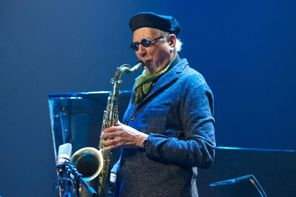 A man in a blue beret and blue jacket playing the saxophone.