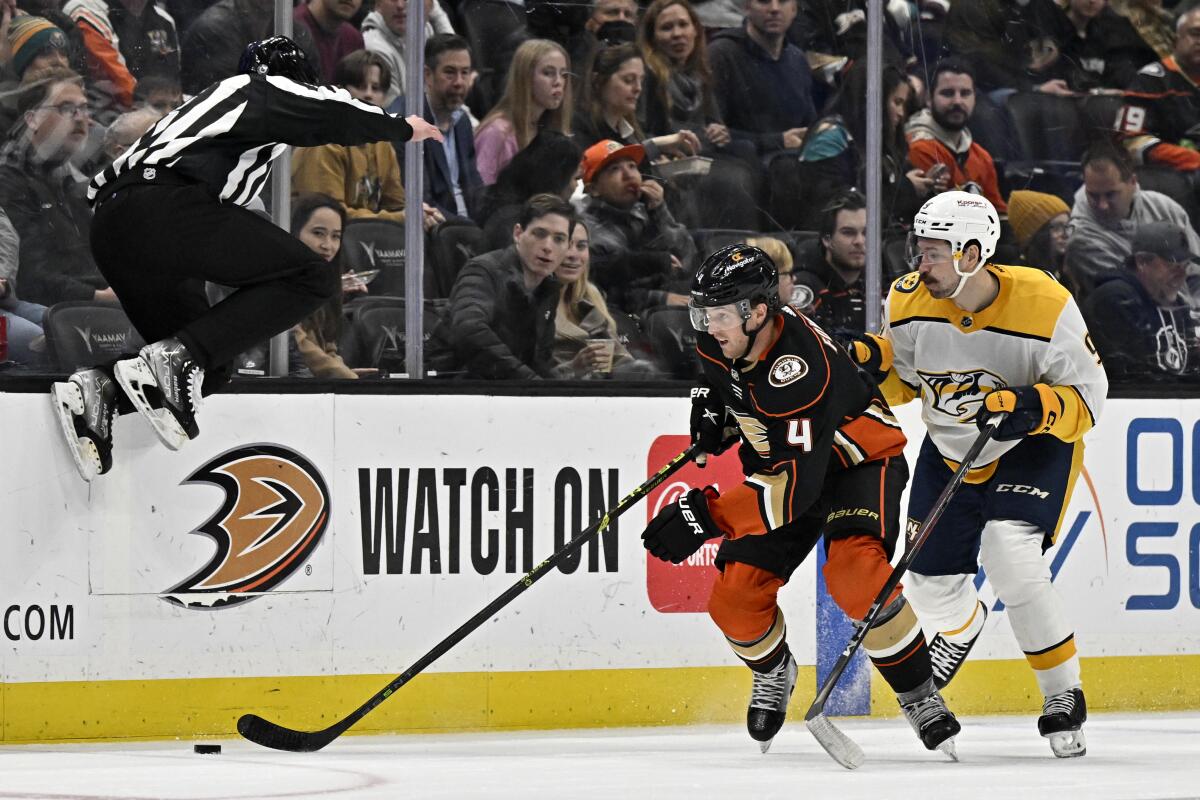 Linesman Kyle Flemington leaps over the puck as the Ducks' Cam Fowler, middle, and the Predators' Filip Forsberg battle.