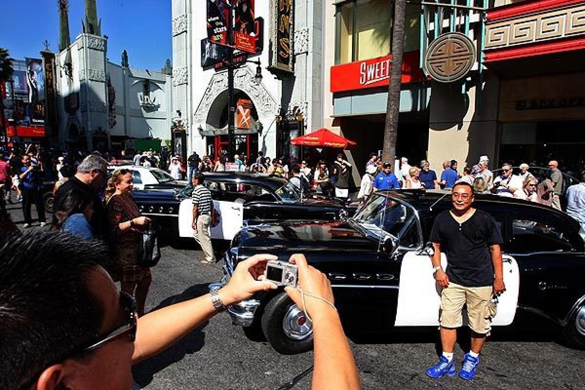 Tourists pose for pictures with vintage police cars on display in Hollywood.