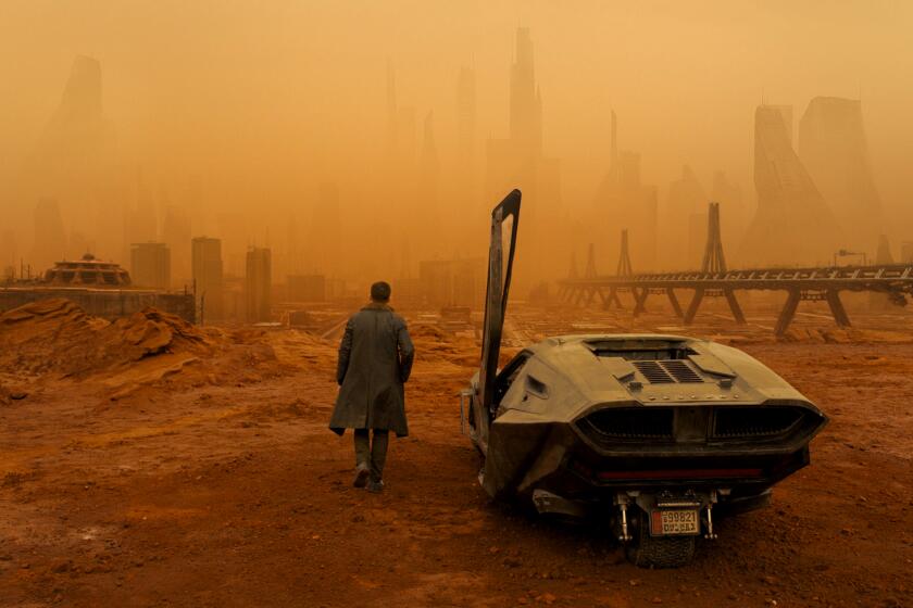 Ryan Gosling walking in a trench coat through an orange, smoggy, desolate cityscape with a futuristic car in the foreground