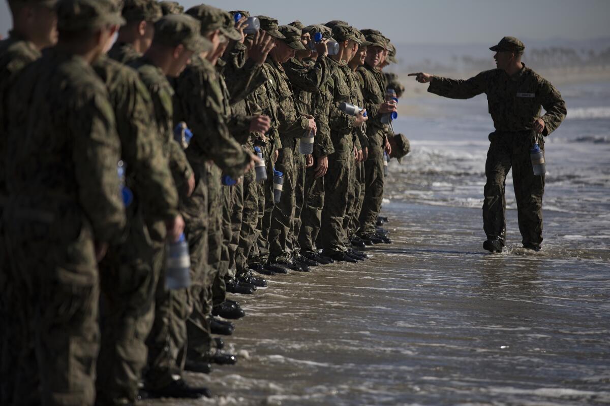 An instructor points at a line of Navy trainees standing at the ocean's edge