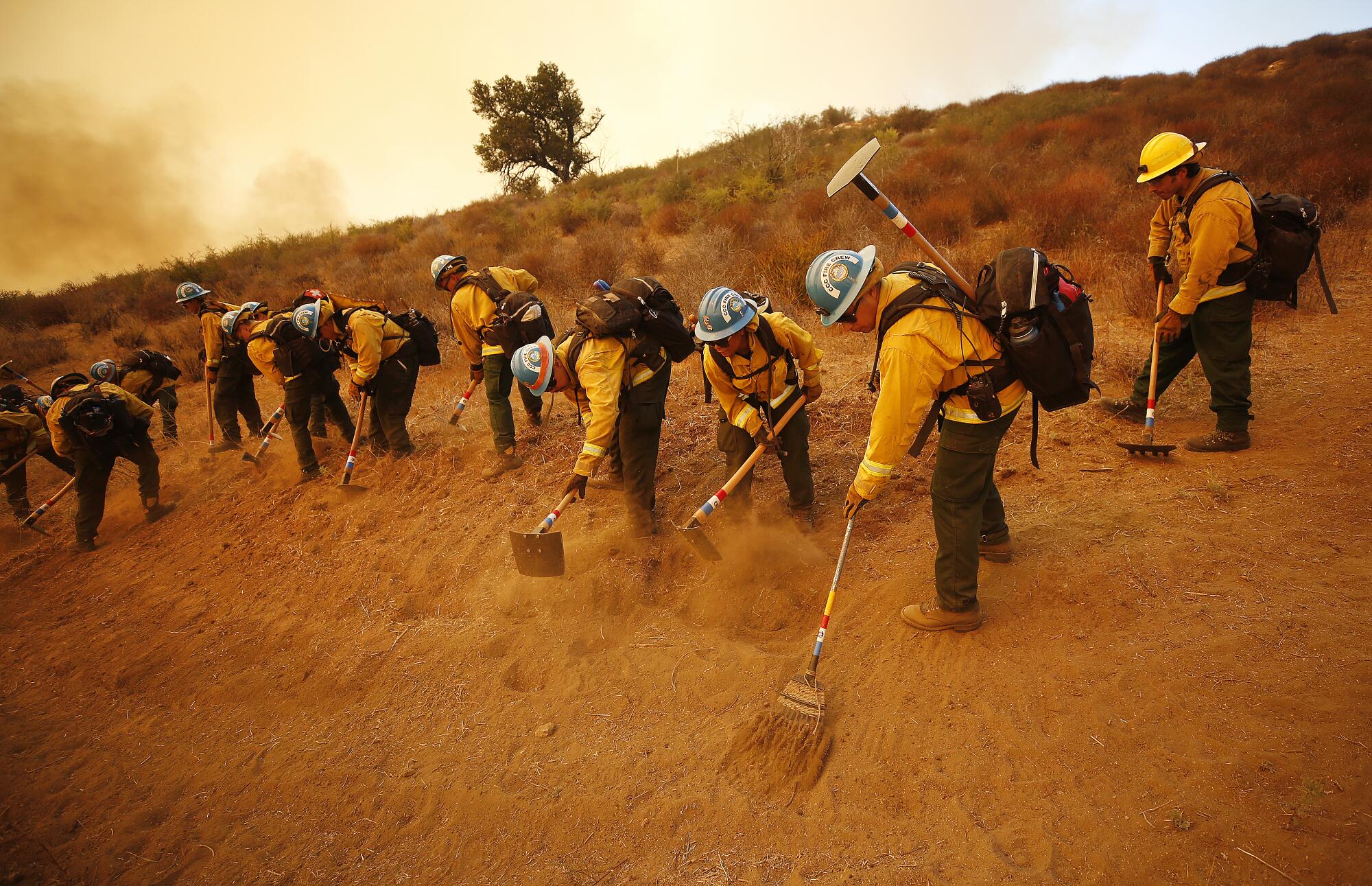 Firefighters rake up earth.
