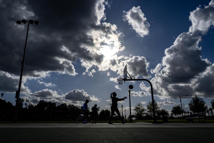 RIVERSIDE, CA - MARCH 29, 2023: The sun peaks through storm clouds bringing out residents to the outdoor basketball court in-between rain storms at Bonaminio Park on March 29, 2023 in Riverside, California. (Gina Ferazzi / Los Angeles Times)